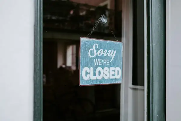 En blå skylt med texten "Sorry WE'RE CLOSED" hänger i ett fönster. Enskild firma i vilande.