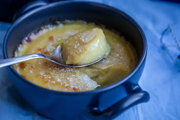 En sked lyfter en bit av krämig, karamelliserad vegansk creme brulee ur en mörkblå skål.