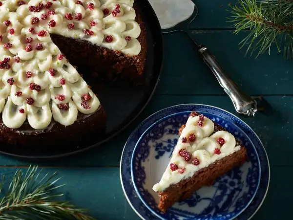 En mjuk pepparkaka med frostning och röda bär. En bit är upplagd på en blåvit tallrik, redo att avnjutas.