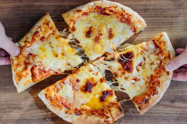 New York Style Pizza mit geschmolzenem Käse, von Händen gehalten, auf Holzuntergrund.