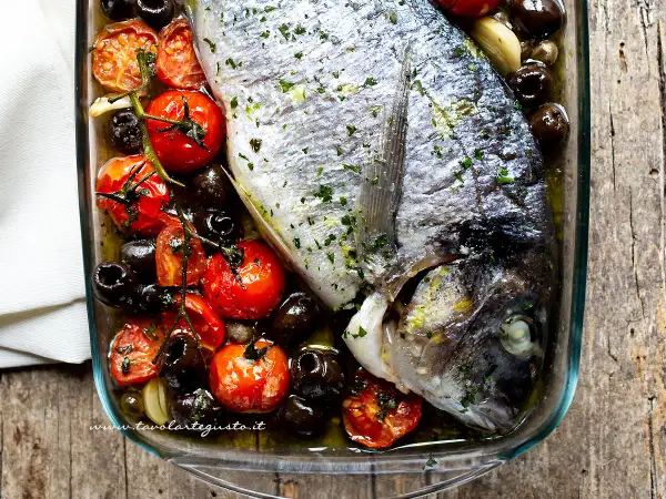 Orata al forno con pomodorini, olive nere e aglio, un piatto semplice e gustoso pronto per essere infornato.