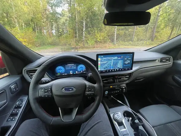 Wnętrze Ford Kuga z nowoczesnym ekranem multimedialnym i cyfrowymi zegarami. Kierownica z czerwonymi przeszyciami i przyciskami.