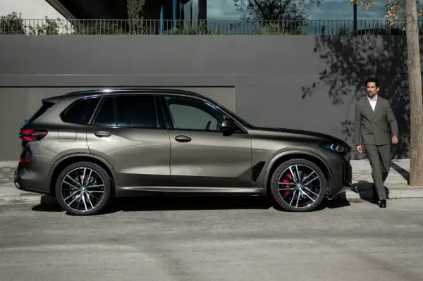 Elegancki mężczyzna w garniturze obok lśniącego BMW G05.