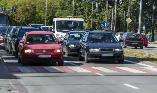 Korki na drodze, kierowcy próbują omijanie stojących aut. Czerwony Volkswagen i granatowa Skoda czekają na zielone światło.