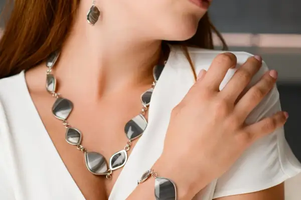 Elegancka kobieta w białej bluzce prezentuje biżuterię z krzemienia pasiastego, kamienia o unikalnym wzorze, który może być Twoim znakiem zodiaku.