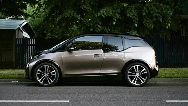 En BMW i3 står parkerad vid en grönskande trädgård. Kanske ett problem med laddningen?