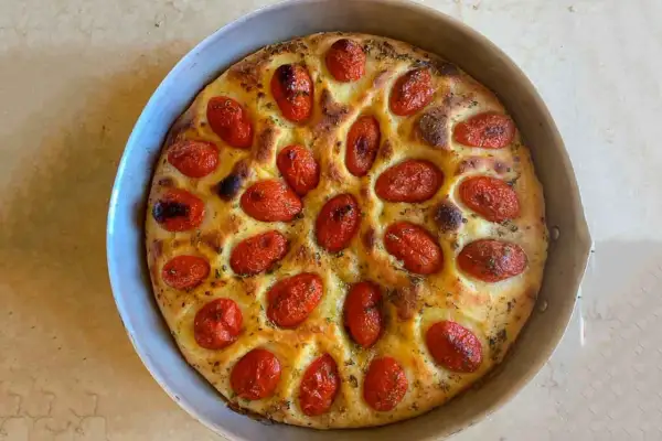 Focaccia foggiana dorata e fragrante, con pomodorini succosi e erbe aromatiche, pronta per essere gustata.