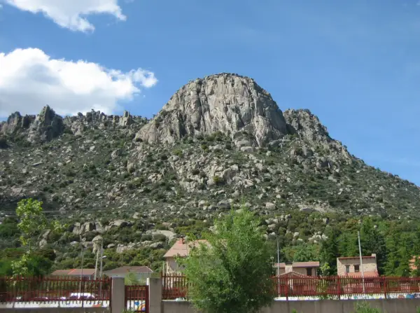 Majestuosa sierra de la Cabrera, con sus rocas imponentes y vegetación verde, bajo un cielo azul con nubes blancas.