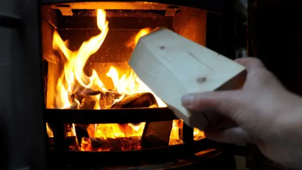 Holzscheit wird in einen brennenden Kamin gelegt. Vorsicht, keine Spanplatten verbrennen!