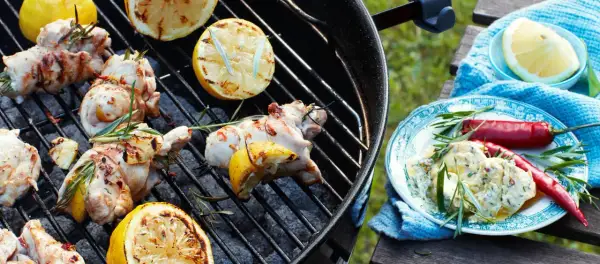 Grillad kyckling med citron och rosmarin på grillen. En tallrik med kycklingröra, chili och örter står bredvid.