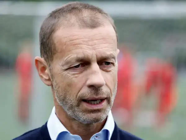 Aleksander Čeferin, prezes UEFA, w niebieskiej koszuli i granatowym swetrze, z rozmytym tłem piłkarzy.