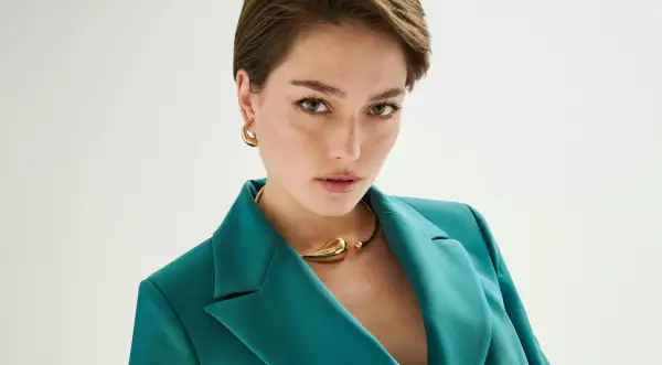 Donna con taglio pixie lungo, indossa blazer verde acqua e collana dorata.