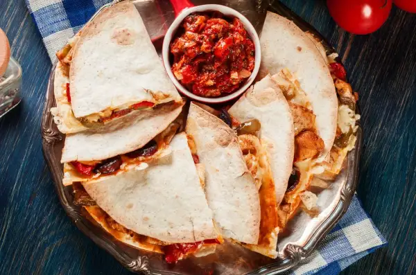Pyszna quesadilla z kurczakiem, podana z salsą na srebrnej tacy. Idealna na szybki obiad.