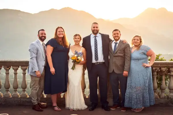 Foto invitati matrimonio: sposi con amici e familiari, con sfondo di montagne al tramonto.
