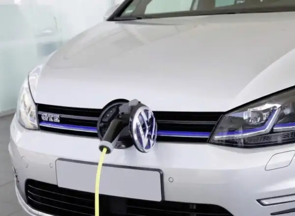 Une Golf 7 GTE blanche est branchée à une borne de recharge. Le câble jaune est visible.