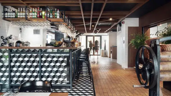Nowoczesny bar w hotelu Almond. Geometryczne wzory na ladzie i podłodze, drewniany sufit, butelki alkoholi na półkach.