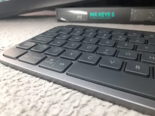 Szara klawiatura Logitech MX Keys S na puszystym dywanie. Klawisz "Enter" jest twardy i gotowy do akcji.