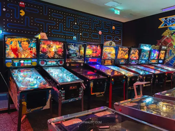 Rząd automatów do gry w stylu retro, w tym maszyny Baywatch i Terminator, tworzy klimat prawdziwego **arcade museum**.