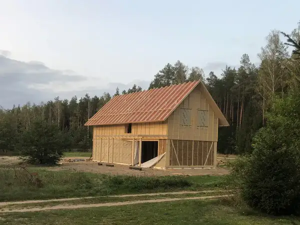 Trwa budowa domu ze słomy. Widać drewnianą konstrukcję, dach i ściany z widocznymi belami słomy.