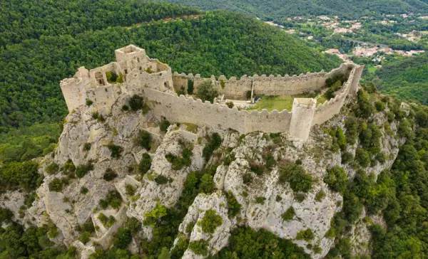 Vestiges d'un château abandonné en Occitanie, perché sur un éperon rocheux, dominant une vallée verdoyante.
