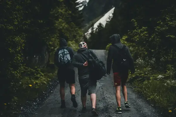 Tres amigos caminan por un sendero boscoso, una aventura perfecta para conocer gente y disfrutar de la naturaleza.