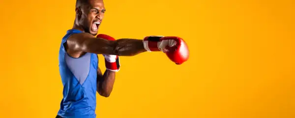 A boxer in a blue tank top throws a punch, his face contorted in a roar. He's ready to compete in the junior welterweight weight class.