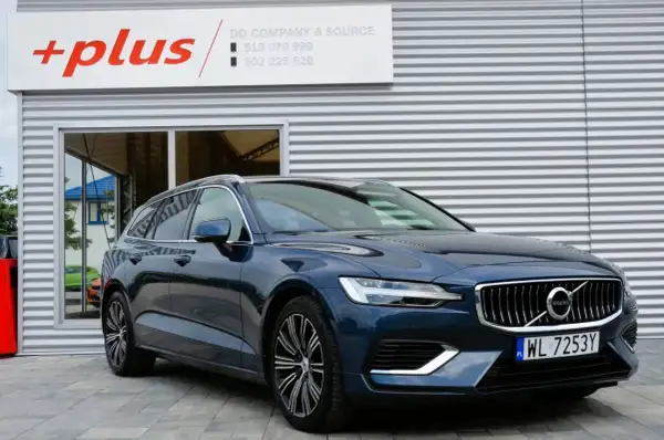 Ciemnoniebieskie Volvo V60 Hybrid z polskimi tablicami WL 7253Y przed budynkiem z logo "+plus".