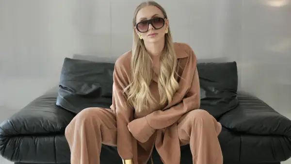 Kobieta w okularach i brązowym komplecie, idealnym do stylu biznes casual, siedzi na czarnej skórzanej kanapie.
