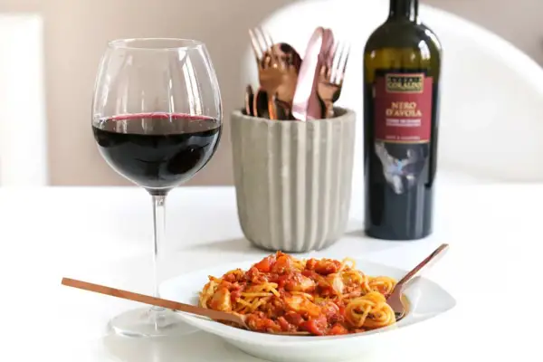Ein Glas Rotwein und eine Portion Spaghetti Bolognese mit einem Hauch von Rotwein. Perfekt für einen gemütlichen Abend.