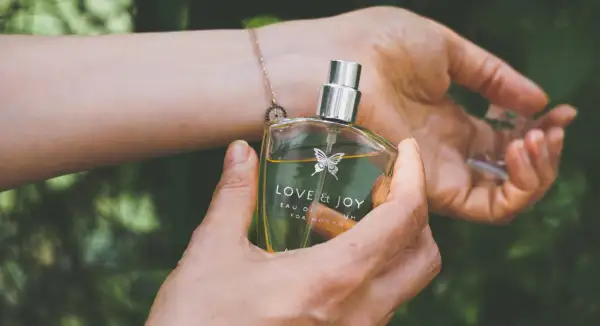 En hand håller en parfymflaska med texten "LOVE & JOY". Doften kan vara en fin present till en parfym gravid.