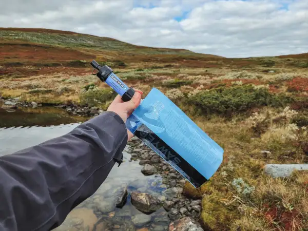 Vattenrening vandring: en hand håller en Sawyer vattenfilterpåse vid en bäck i fjällterräng.