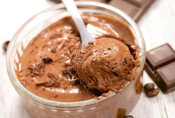 Une cuillère prélève une portion aérienne de mousse au chocolat, garnie de copeaux de chocolat. Un délice gourmand.