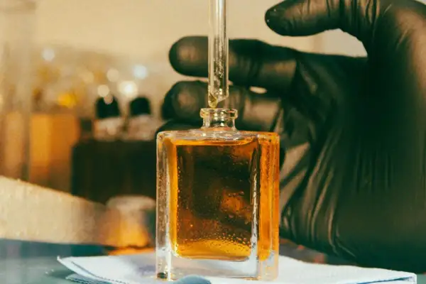 Kropla płynu, zawierającego cenną **molecule**, spada z pipety do kwadratowej buteleczki.
