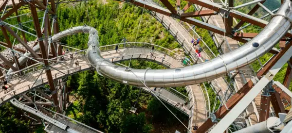 Drewniana ścieżka w koronach drzew z metalową zjeżdżalnią, widok z góry na Sky Walk w Czechach.