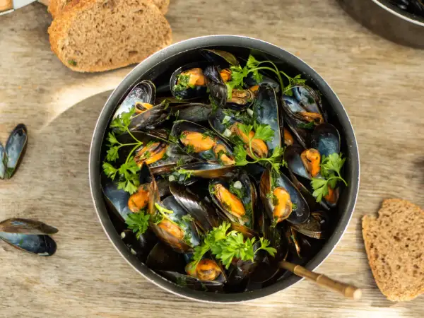 Un plat généreux de moules marinières, garni de persil frais, servi avec du pain de campagne sur une table en bois.