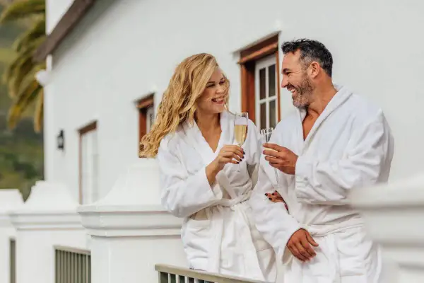 Para, ubrani w szlafroki, wznoszą toasty szampanem na balkonie. Zastanawiają się, ile kosztuje noc w hotelu, ciesząc się luksusem.