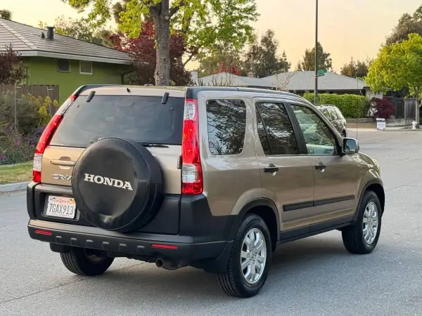 En gyllene Honda CRV 2005 står parkerad på en gata, med reservhjulet synligt på bakluckan.