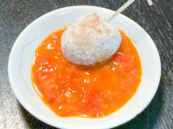 En boll med potatis doppad i en kryddig mojo rojo-sås.