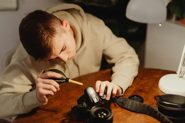 A young person carefully performs camera cleaning, using a blower to remove dust from their DSLR.