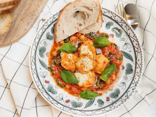 En tallrik med ricotta recept: smakliga ricotta-bollar i tomatsås med kikärtor, spenat och basilika, serverad med rostat bröd.