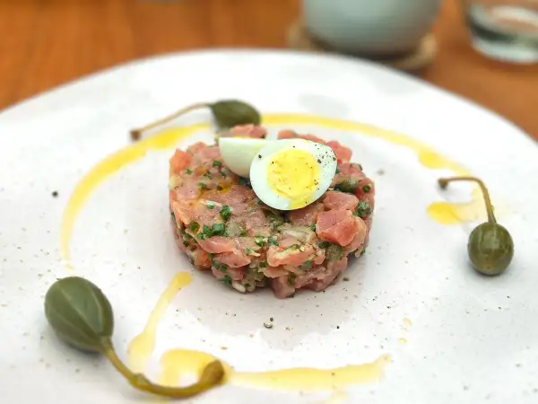 Un délicieux tartare de thon, garni d'un œuf de caille et de câpres, est servi sur une assiette blanche avec un filet d'huile d'olive.