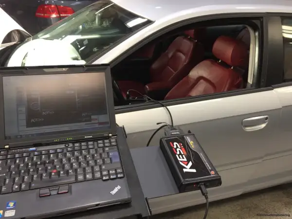 Laptop och KESS-enhet kopplade till en bil för att chippa bilen. Röd läderinredning syns i kupén.