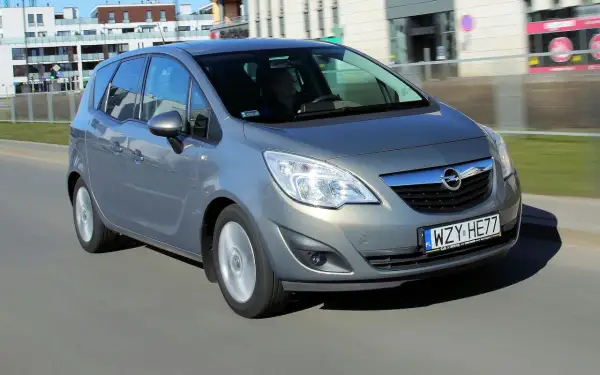 Szary Opel Meriva B w ruchu miejskim, z widocznym kierowcą za kierownicą.