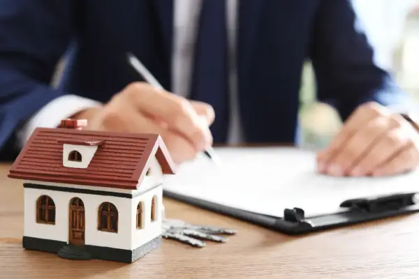 Modellino di casa, chiavi e un uomo che firma un documento. Scopri cos'è la rendita catastale per la tua casa.