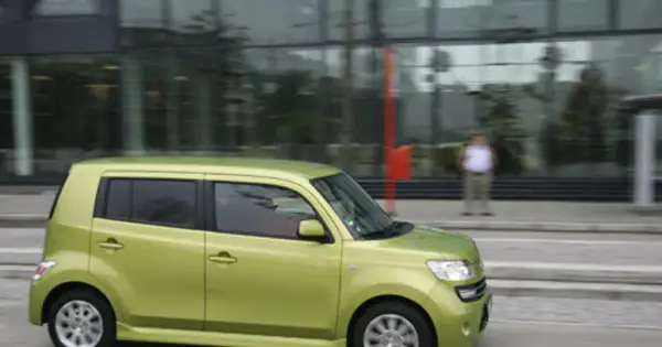 Zielony Daihatsu Materia jedzie ulicą obok nowoczesnego budynku.