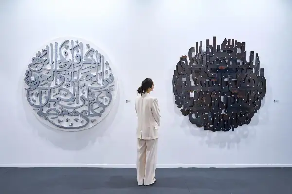 En kvinna i ljus kostym betraktar två runda konstverk med arabisk kalligrafi. Det vänstra är i metall, det högra i mörkare material. En atra daniel.