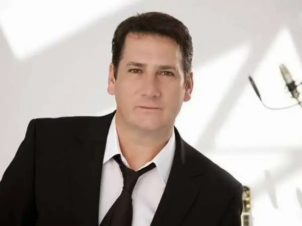 Tony Hadley, uno dei membri dei Spandau Ballet, in giacca e cravatta, con un microfono sullo sfondo.