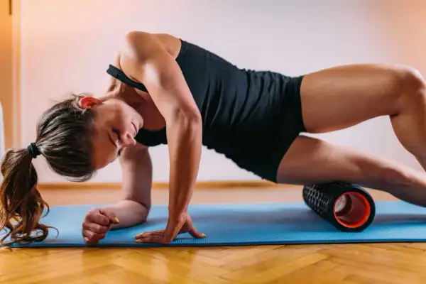 Woman performing a full body foam rolling routine on a blue mat, targeting her quadriceps.