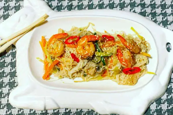 Deliziosi spaghetti di riso con gamberi succulenti e verdure croccanti, guarniti con semi di sesamo.