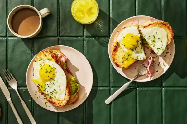 Två läckra croque madame med stekt ägg, ost och skinka, serverade med kaffe och juice.
